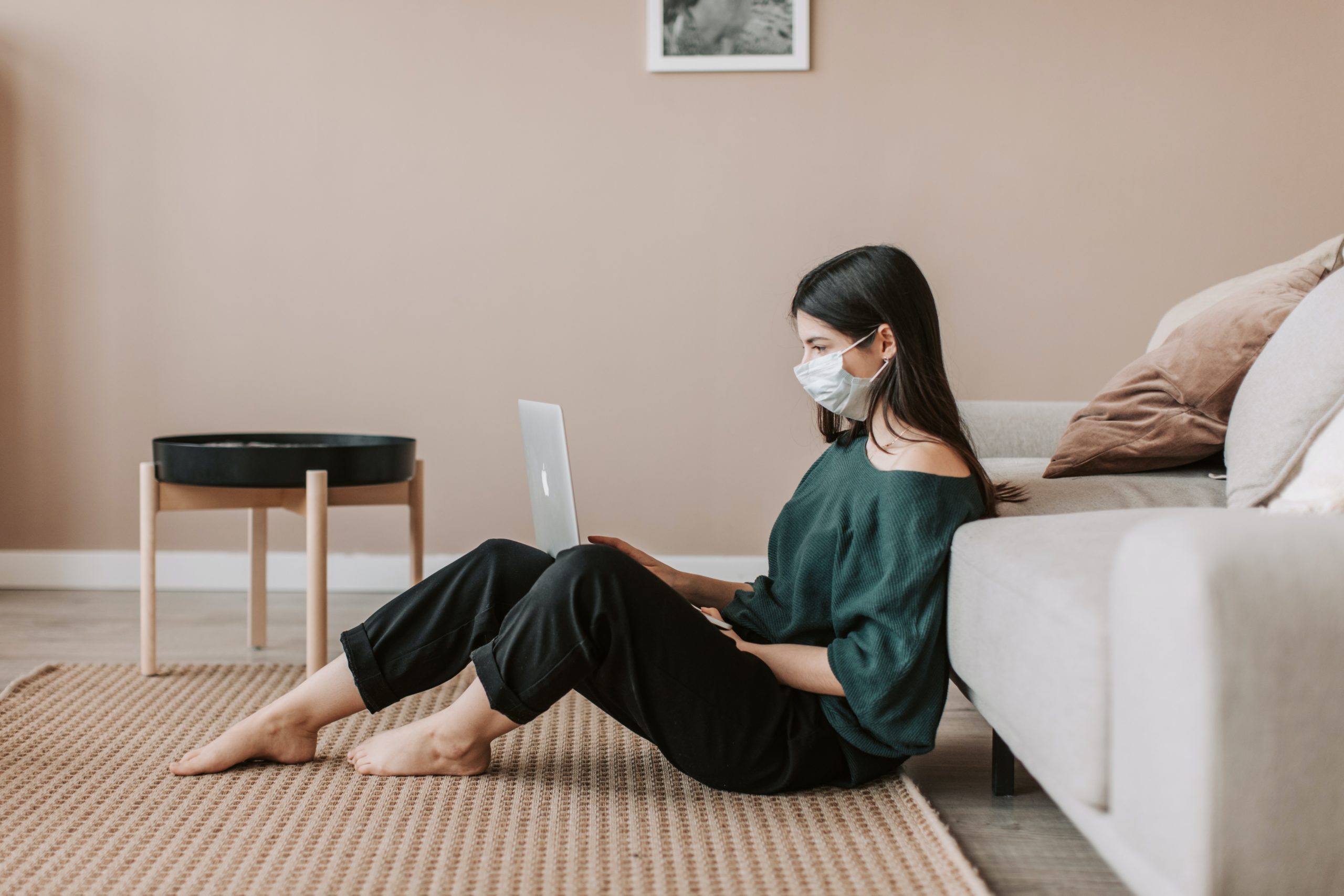 Female in face mask sitting on a floor on her laptop
